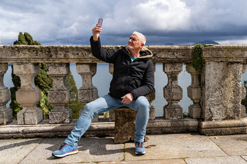 happy middle aged traveler man on vacation taking a selfie on an outdoor terrace facing lake...