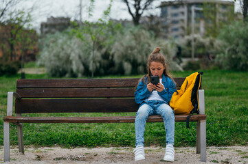 Beautiful little boy using smart phone in the park.