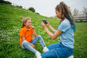 A boy accompanied by his older sister using a smartphone sitting in the garden.