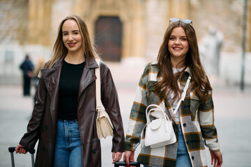 Two female tourists explore a European city, pulling their suitcases along as they wander through...