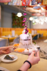 A hand holds a very exotic plate with various types of sushi and sashimi against a warm and colorful Japanese restaurant backdrop. Dry ice smoke falls, creating a beautiful effect