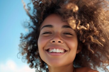 portrait of curly smiling woman with flying hair, sunny day, blue sky