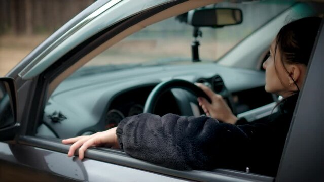 Young 30s woman driving car through forest. Side view female driver holding steering wheel. Female learn driving and traveling alone. Shooting from outside