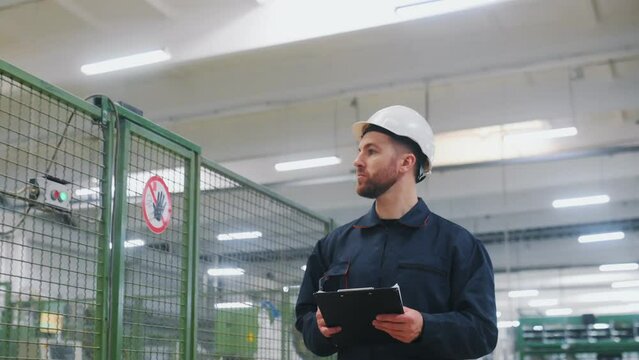 Employee engender in uniform and with white hard hat walks in the factory.