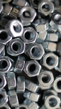 Many stainless hex nuts rotating close-up. Metal industry concept. Vertical video.