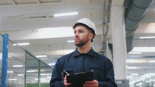Employee engender in uniform and with white hard hat walks in the factory.