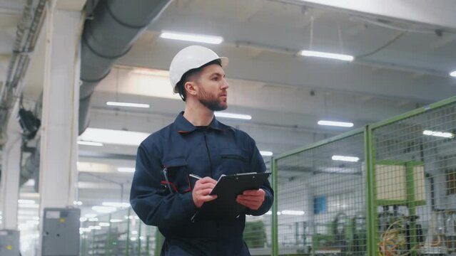 Employee engender in uniform and with white hard hat walks in the factory.