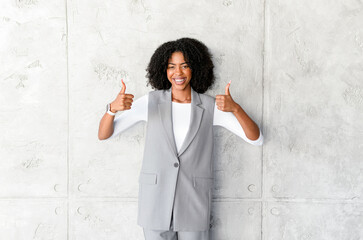 A beaming African-American businesswoman gives a double thumbs up, signaling approval and success,...
