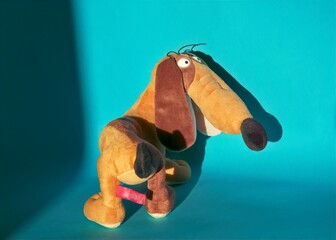 close-up of a half-turn soft toy of a funny light brown dachshund on a blue background with a shadow on the wall