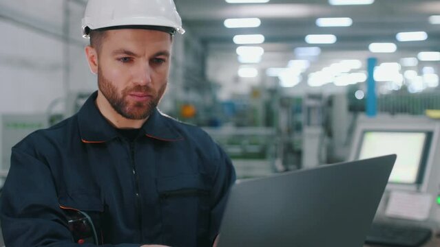 Using the laptop. Factory worker is indoors with hard hat.