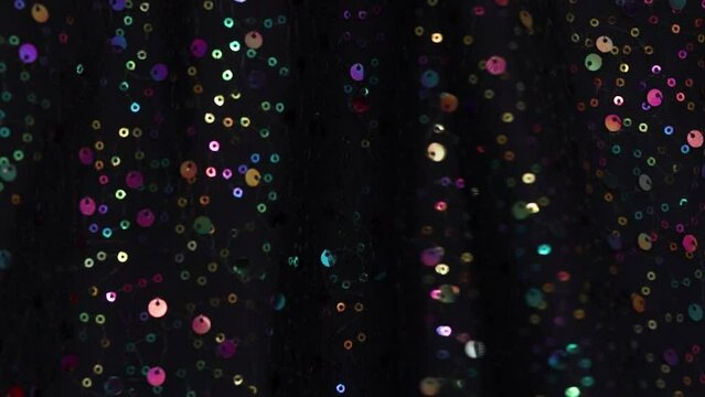 background of multi-colored shiny sequins on a black background. Dynamic sparkling of multi-colored lights on a dark background. Draped shiny expensive fabric for festival celebration.