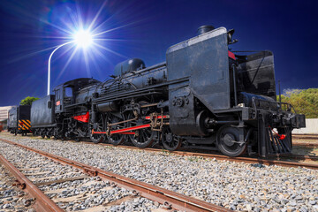 At night, the old steam locomotive is illuminated by modern street lights, forming an interesting...