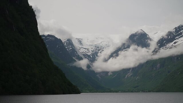 tranquil and calm Oldevatnet glacial lake in front of the melting Briksdalsbren glacier in Norway with snow capped mountains.