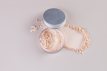 Open cosmetic jar with silver lid with delicate loose powder on pastel background with powder swatch. Top view. A copy space.