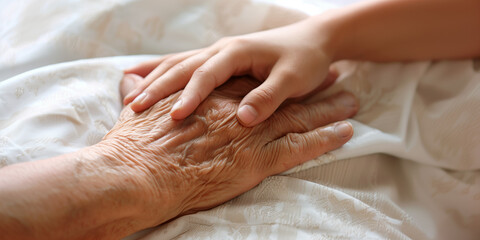 A young hand touching an old hand on a bed, helping and caring for the elderly, end of life support, solidarity and assistance for aging people