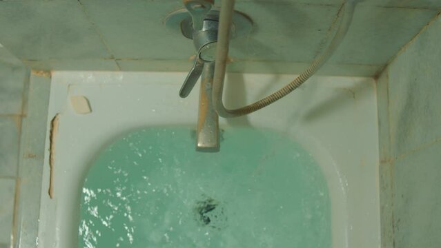 Old bathtub with running water from a rusty faucet, depicting neglect or the need for renovation.