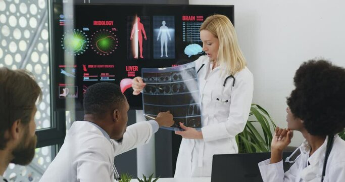 Medical colleagues advising together with their woman head doctor while previsioning x-ray image. Medical concept.
