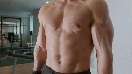 Portrait of young handsome man in gym who shows off his big muscles and abdominal. Slow motion. Sports and healthy lifestyle concept
