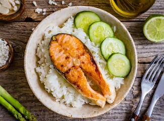 Seared salmon steak with boiled white rice and sliced cucumber on wooden table top view