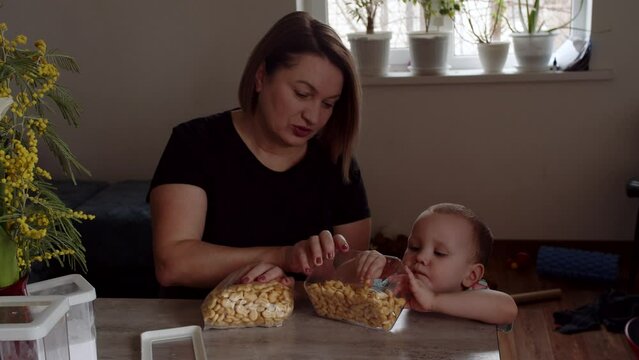 Mom with a kid taking cookies out of a bag on the table.