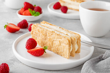 Traditional French dessert millefeuille with vanilla cream and fresh berries on a white plate on a gray concrete background.