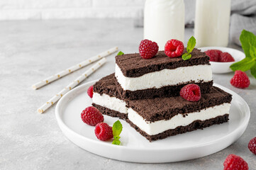 Chocolate cake with milk cream filling on a white plate with fresh raspberries and mint with bottles of milk. Delicious dessert. Copy space.
