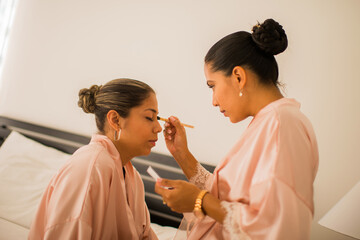 mujeres jovenes latinas frente a frente una de ellas ayudando a maquillar a su compañera 