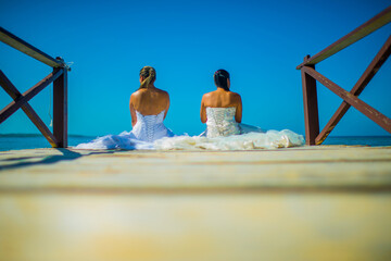 mujeres sentadas dando la espalda mientras usan sus vestidos de boda y miran en mar en el muelle 