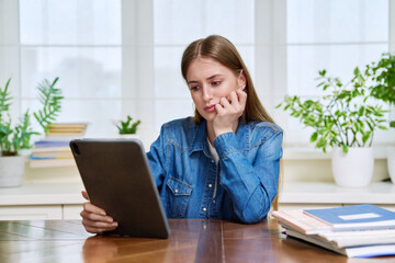 Teenage female student at home looking talking in web camera of digital tablet