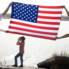 large American flag, child stands under it and looks into the distance through binoculars. Independence Day. National symbol of freedom of the States of America. Bright future., travel across America