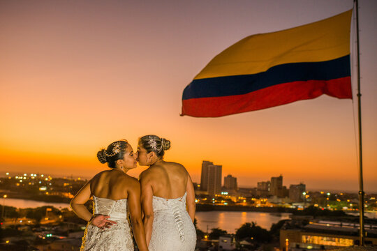 mujeres jovenes besandose en el atardecer junto a la bandera de colombia y un fondo de la ciudad