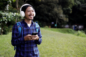 Young Asian man in a casual outfit, wearing a beanie, blue plaid shirt, and headphones, checks his...