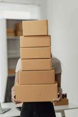 Freelance Asian woman wearing an apron uses laptop and boxes to take and check online orders to...