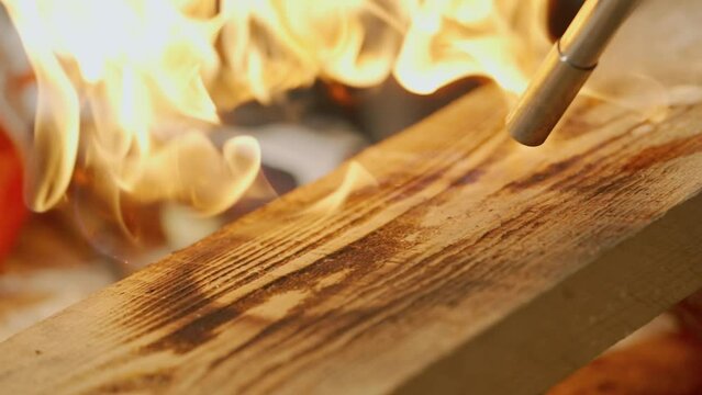 Male woodworker working in garage. Man professional carpenter working with wooden materials in workshop burning piece of wood with gas torch, close up.