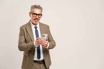 The grey-haired mature businessman smiles and looks at the camera while using his smartphone, showcasing a senior professional comfortably navigating modern communication technology