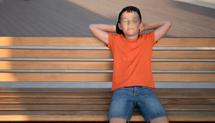 A cute boy sits on a bench and dreams, rests.