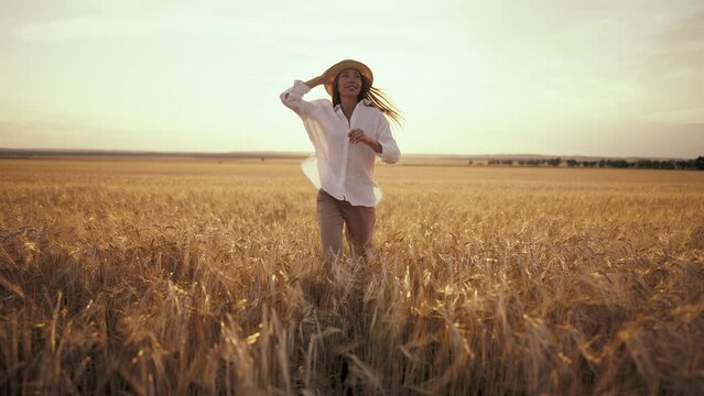 Romantic carefree happy woman running on yellow wheat field with spreading flying arms enjoying freedom calmness on rural nature during vacations holidays. Rest, activity in country, peace at sunset.
