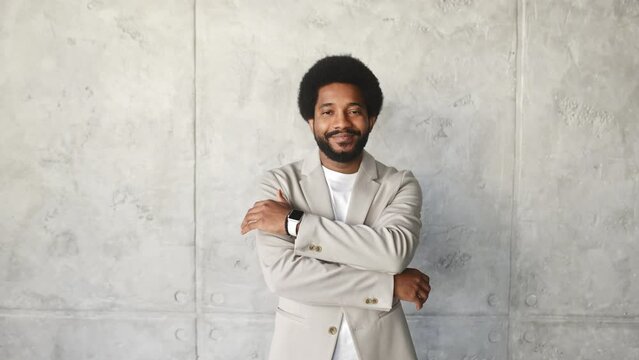 A confident smiling businessman stands arms crossed against a concrete backdrop, exuding a blend of casual charm and professional strength. Successful, approachable leadership in a modern business