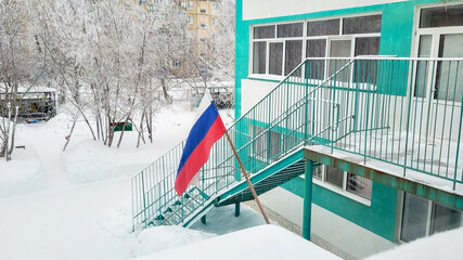 Russian flag in the snow above the entrance to the kindergarten building in winter.