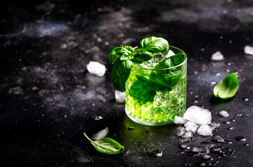 Green summer alcoholic cocktail drink with dry gin, sugar syrup, lemon, green basil and ice, dark...