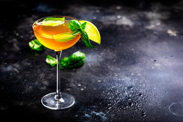 Spring orange cocktail drink with scotch whiskey, apple liqueur, ginger, lemon juice, green basil...