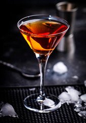 Orange alcoholic hard cocktail drink with scotch whiskey, vermouth and liquor in martini glass, dark bar counter background