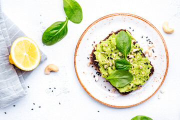 Avocado toasts with spinach and cashew nuts sprinkled with sesame seeds on white table background,...