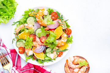 Fresh delicious shrimp salad with orange, lettuce, tomatoes, cucumbers, onions and sesame seeds with olive oil, white background, top view - 779781961
