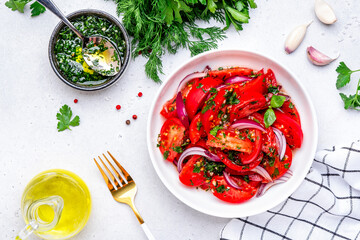 Fresh juicy summer tomato salad with parsley garlic and olive oil dressing and red onion, white table background, top view - 779781962