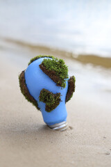 social problems. Earth Day. blue light bulb with green moss in the sand on the seashore