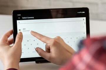 Woman finger of hand choosing foreign CHF, swiss franc currency from the list on the tablet for buying choosing online shopping, booking hotel