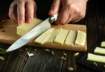 Chef hands close-up with a knife cutting cheese for placement on a sorting board.