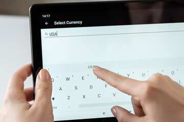 Woman finger of hand choosing foreign USA, dollar currency from the list on the tablet for buying...