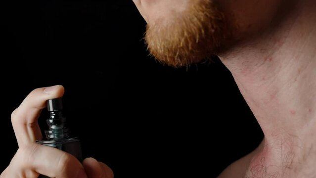 A black cologne bottle, a man with a red beard spraying it on himself.